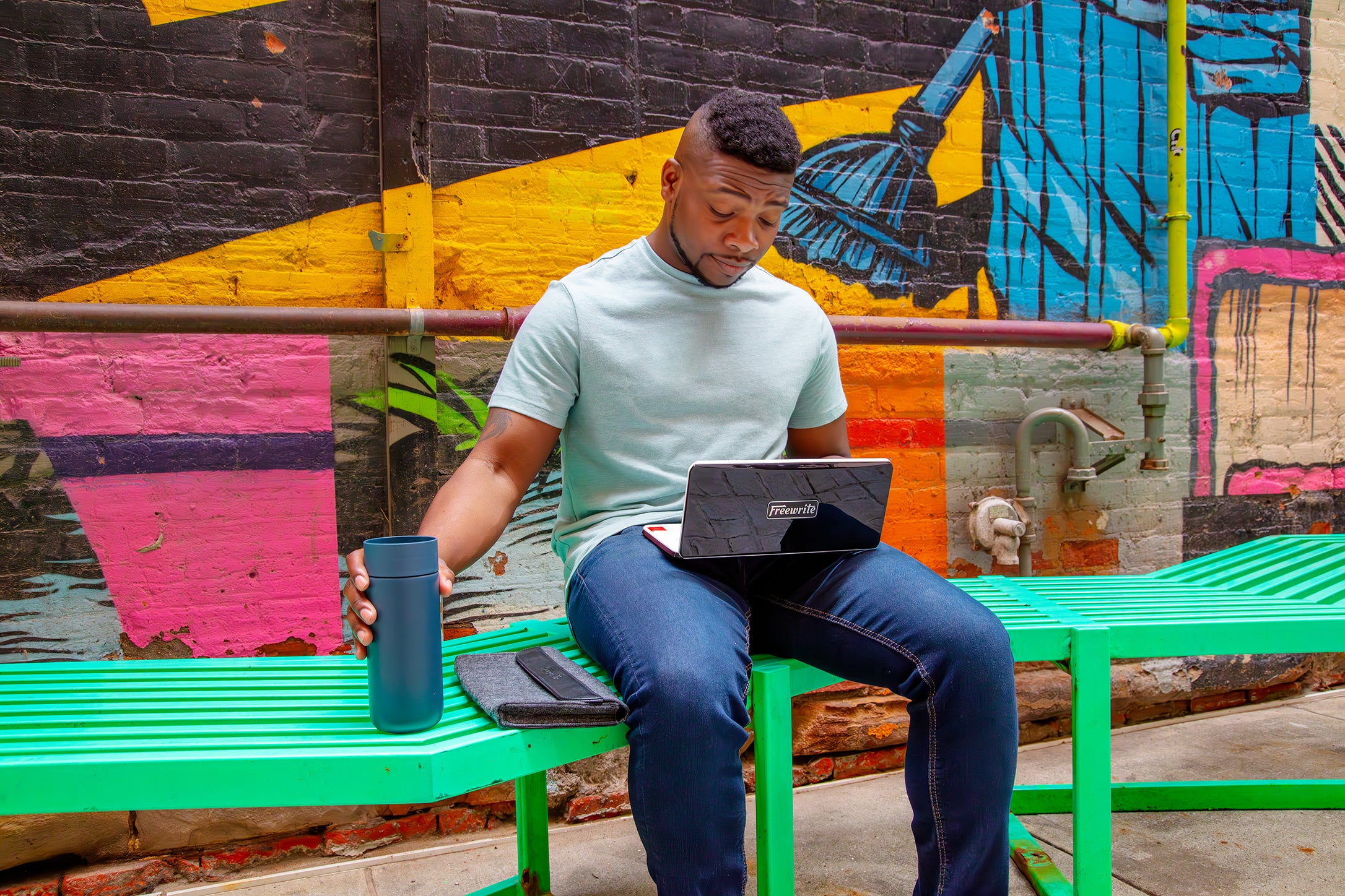 Man sitting with laptop on colorful urban bench.