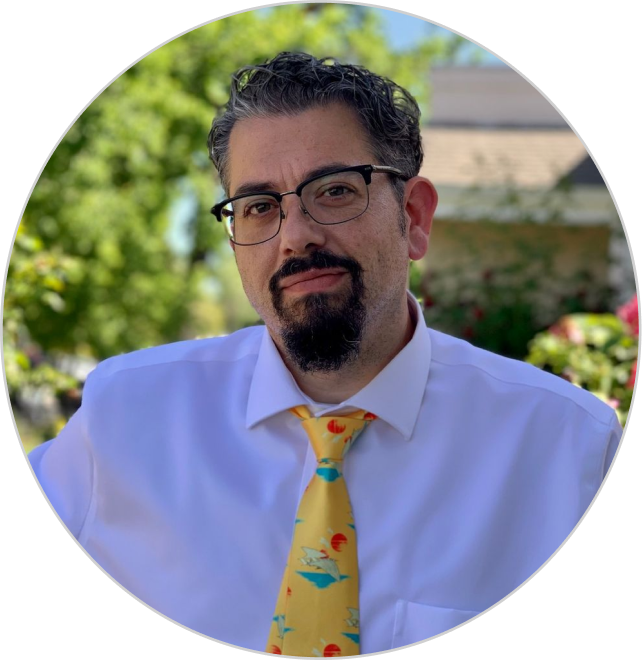 Man with glasses wearing a white shirt and yellow tie with chili pepper pattern.