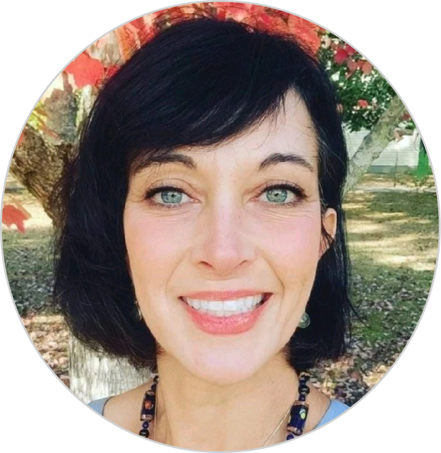 A smiling woman with dark hair and earrings, outdoors with trees in the background.