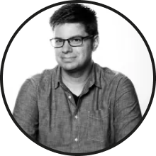 Black and white portrait of a smiling man wearing glasses and a shirt.